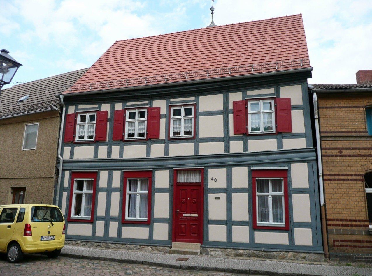 A yellow car is parked in front of a house with red shutters