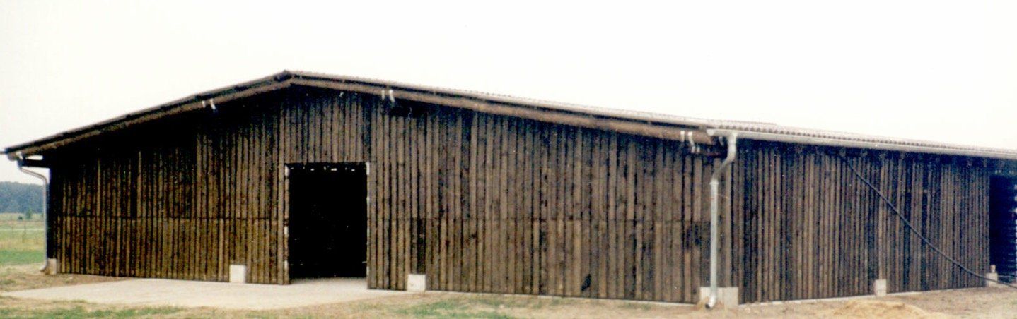 A large wooden barn is sitting in the middle of a field.
