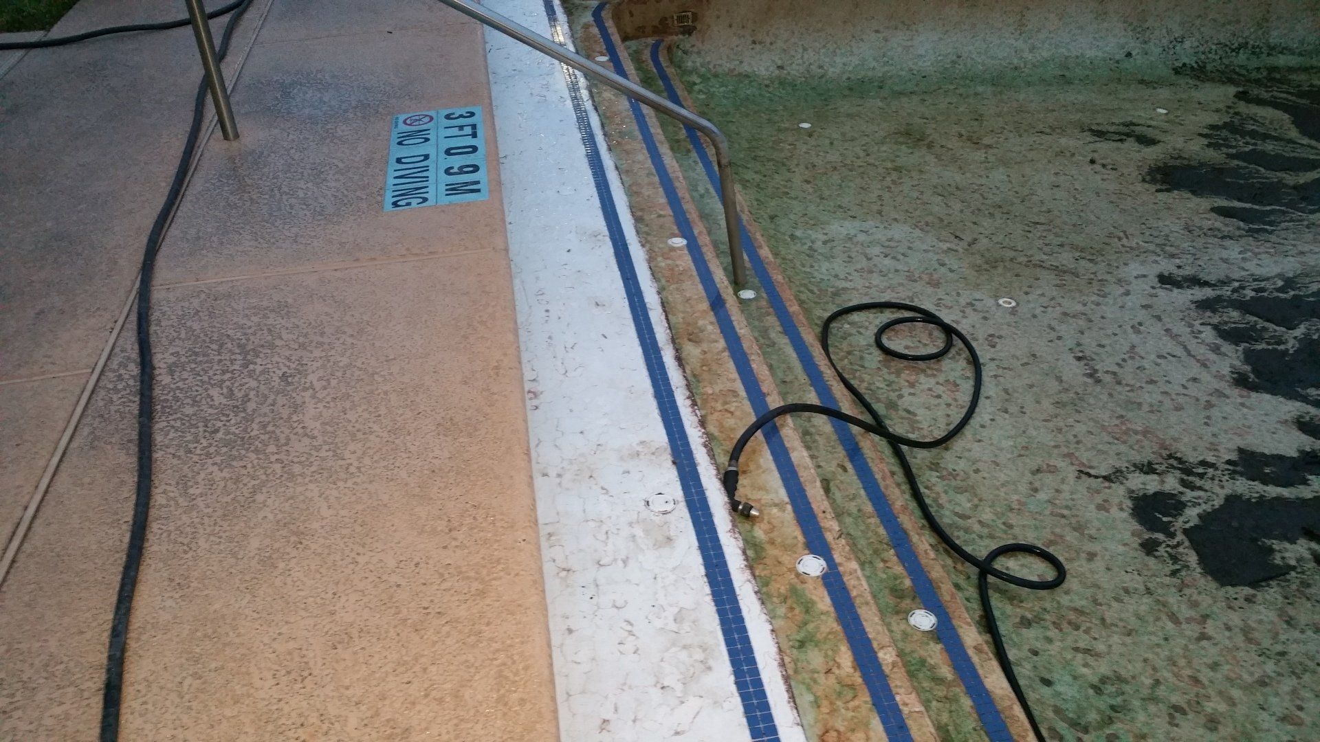 Textured pool deck beside a blue-tiled pool edge with a hose and wet concrete nearby