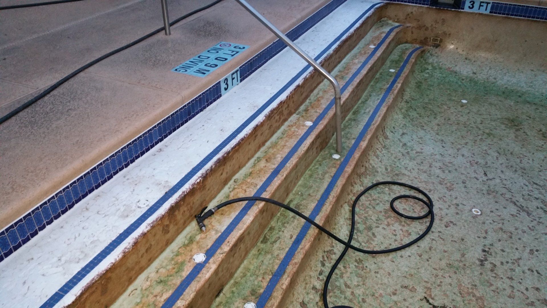 Coiled black cable beside a pool edge with blue safety lines and tiled deck walkway