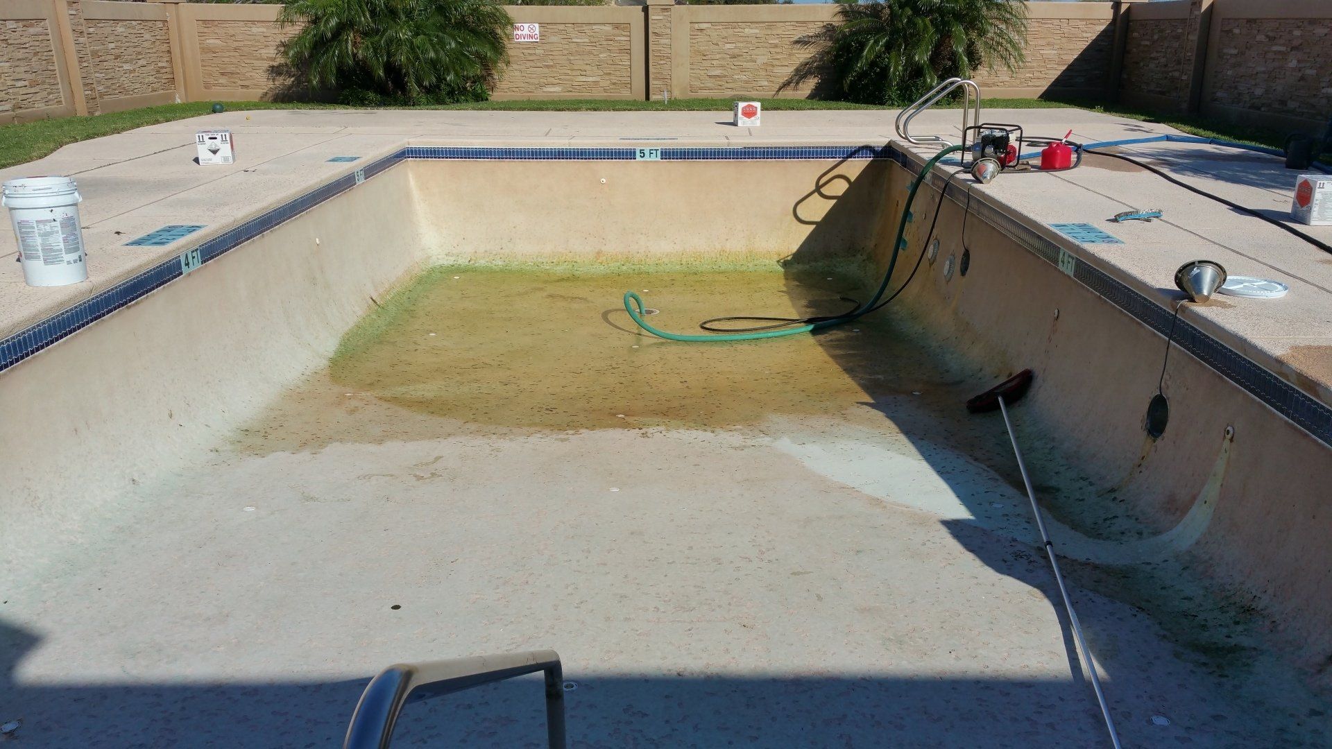 Empty drained swimming pool with stained walls and debris in the basin