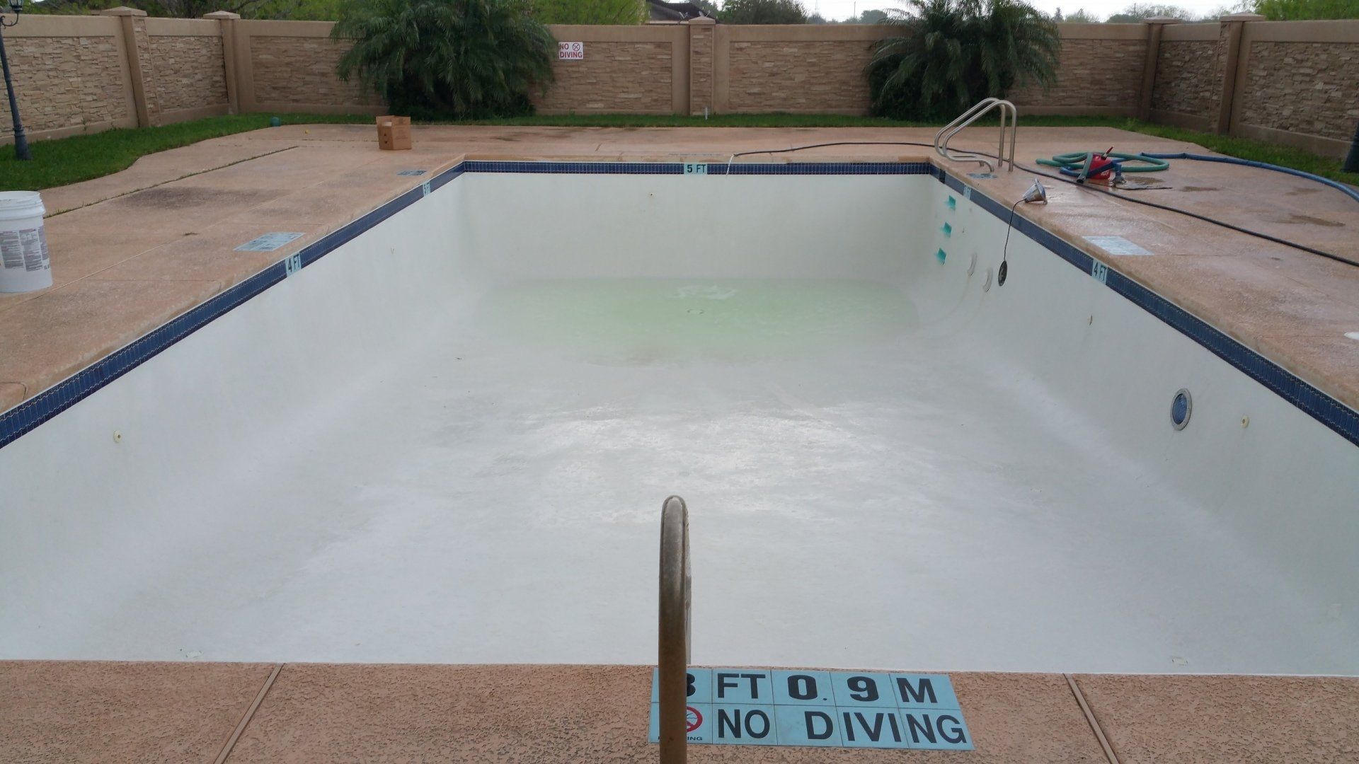 Empty swimming pool with a white interior, beige deck, and a “NO DIVING” sign at the edge.