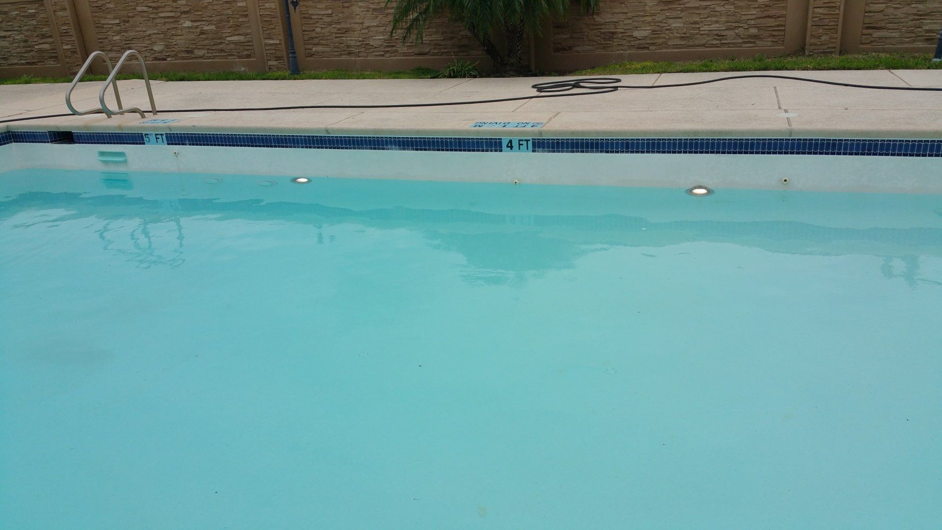 Swimming pool with turquoise water and a stone deck beside a brick wall