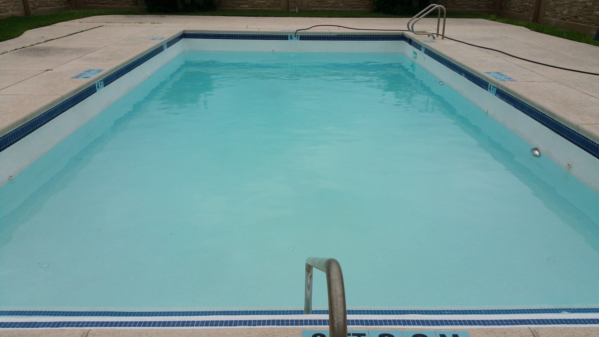 Empty outdoor swimming pool with clear blue water and ladder at the near edge