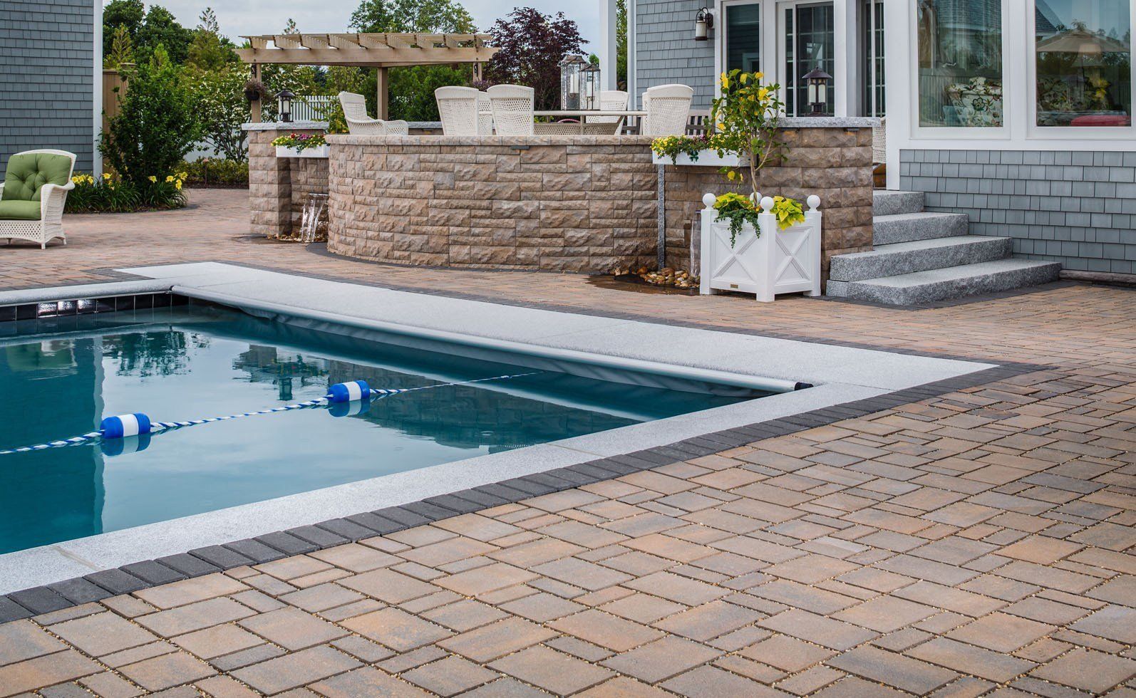 Modern backyard patio with a swimming pool, stone deck, and white outdoor seating area