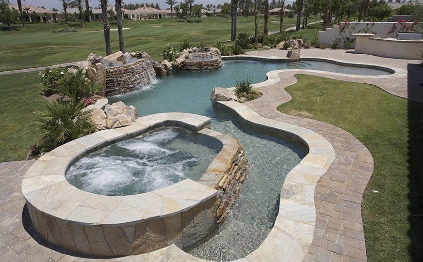 Curved outdoor stone water feature with small pools and a landscaped grassy area