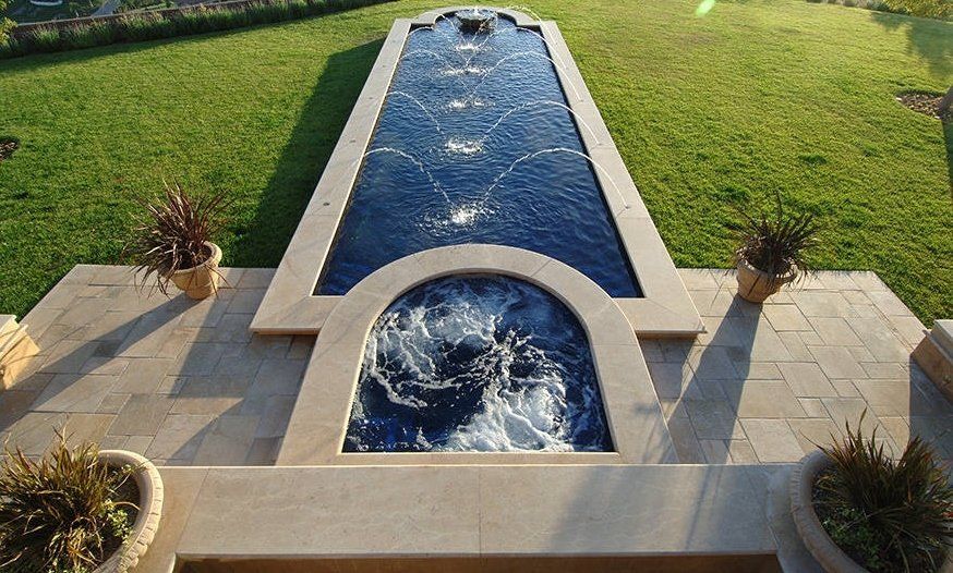 Rectangular backyard pool with a circular spa and blue water, bordered by stone paving and green lawn