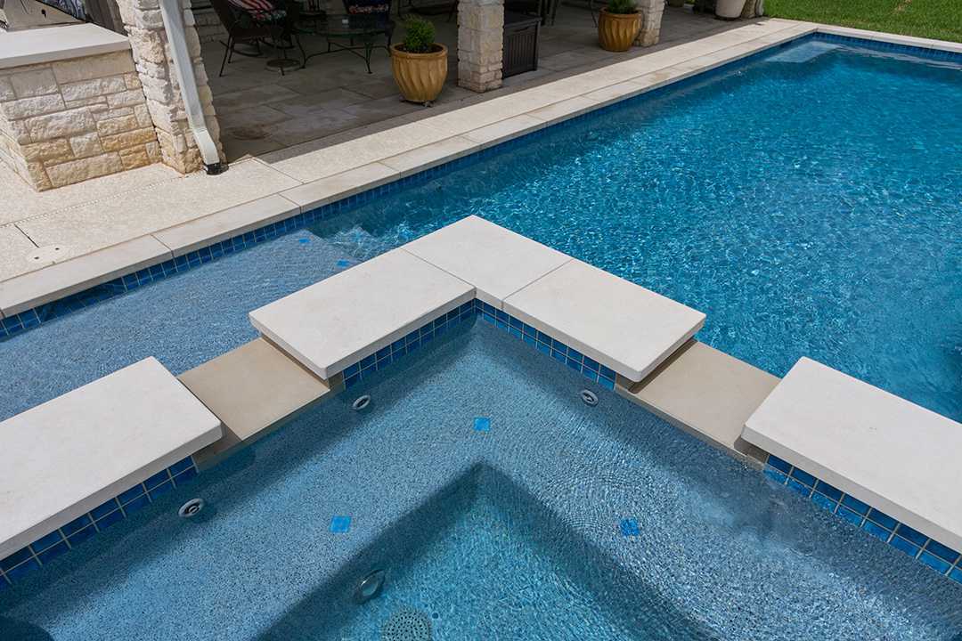 Blue swimming pool with white lounge platforms and stone patio seating area