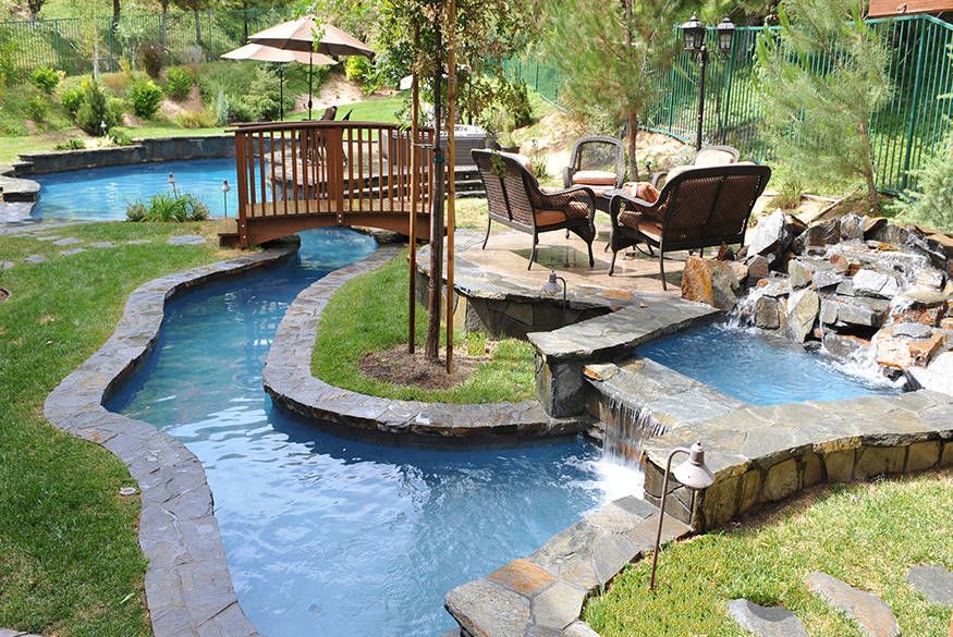 Backyard stream and waterfall with a small bridge, patio chairs, and lush landscaping