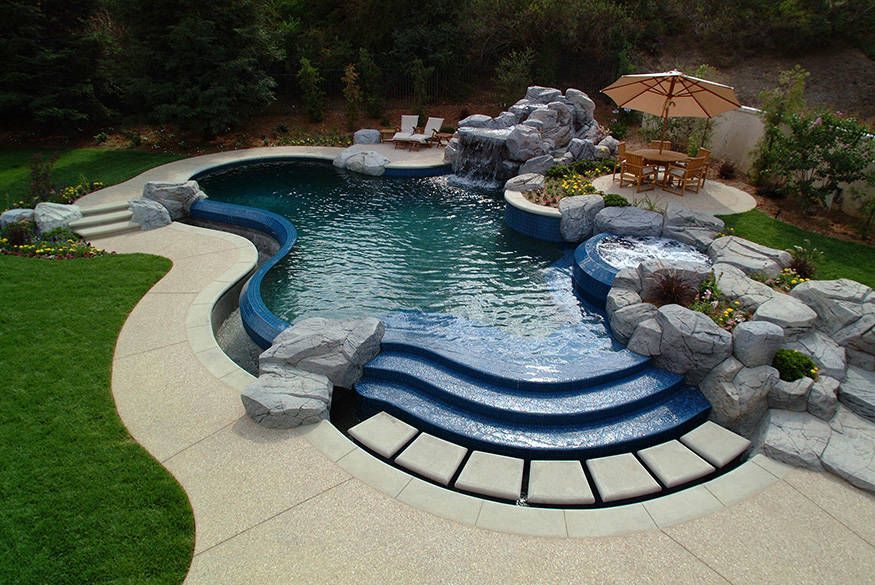 Curved backyard swimming pool with rock features, blue steps, and a patio area