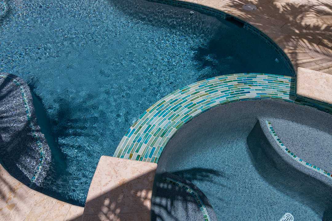 Blue tiled swimming pool with a curved mosaic walkway and palm shadows