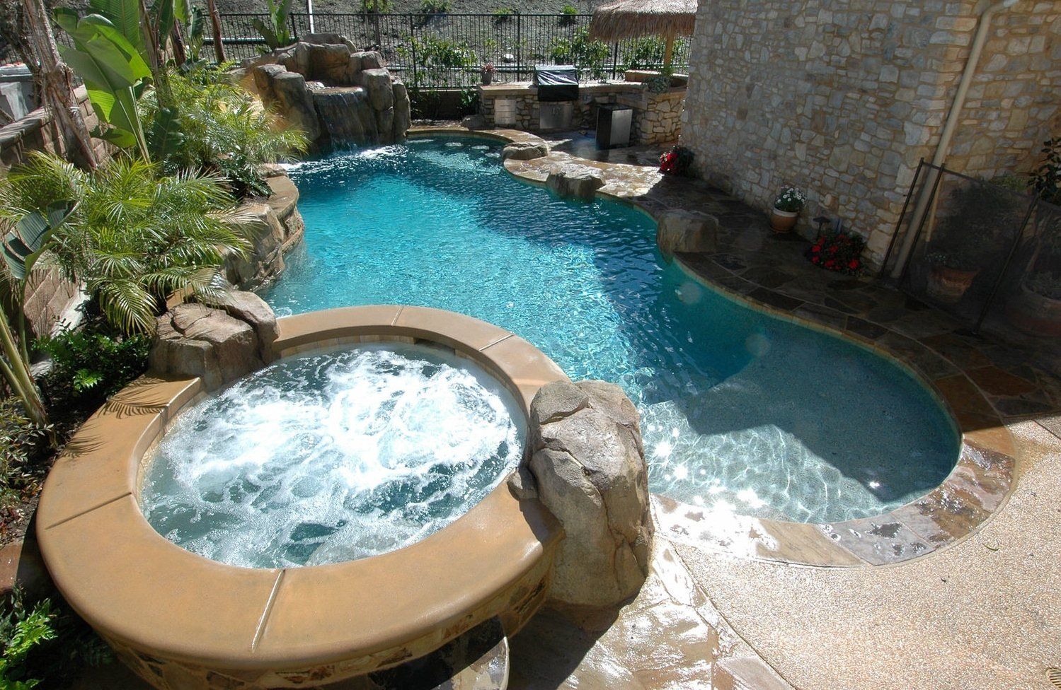 Backyard pool with a bubbling hot tub and turquoise water beside stone landscaping