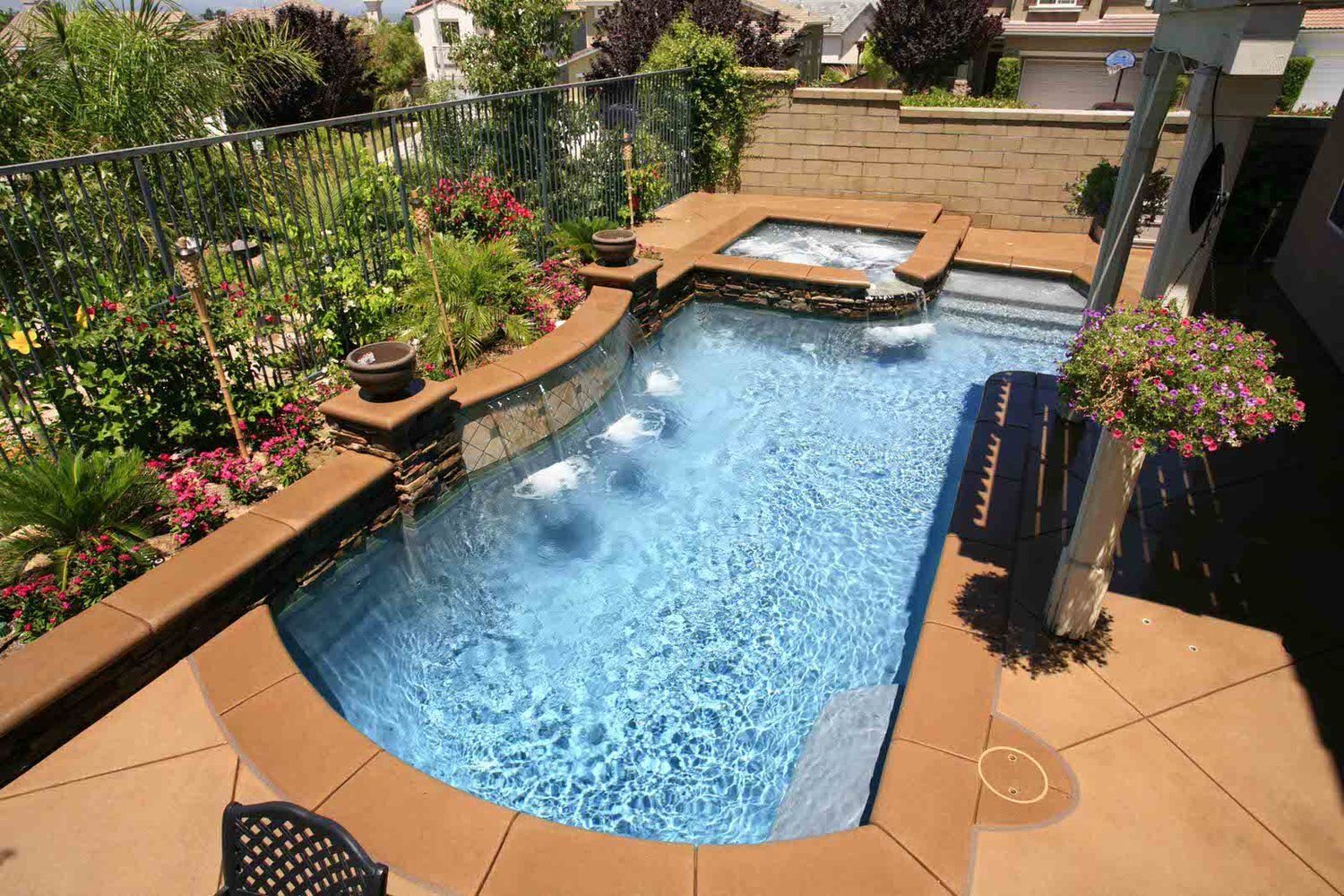 Backyard swimming pool with blue water, stone decking, and lush potted plants in a landscaped patio.