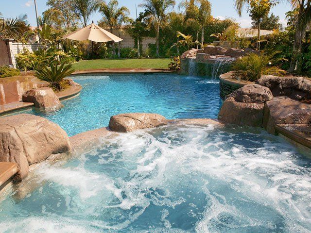 Tropical backyard pool with a rock waterfall, palm trees, and a shaded lounge area