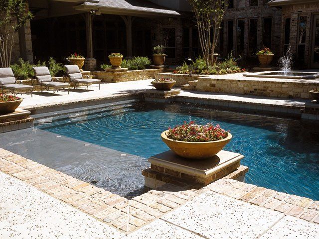 Courtyard pool with blue water, stone deck, and a flower planter on a pedestal.