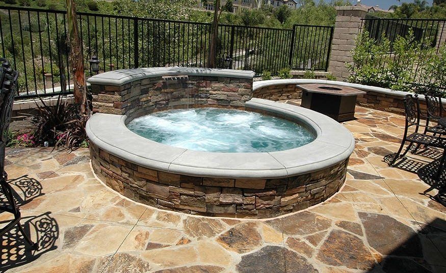 Stone hot tub with bubbling water on a flagstone patio, set against a fenced desert landscape.