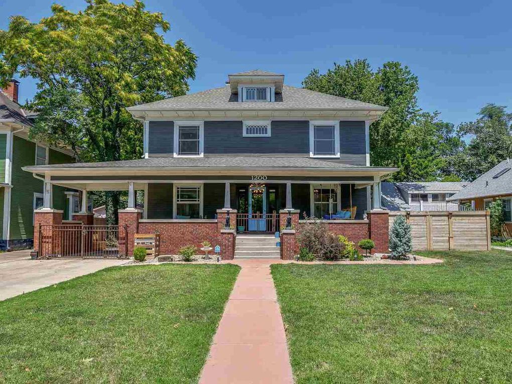 Two-story blue house with porch, brick accents, and green lawn under a sunny sky.