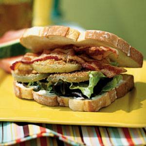 BLT sandwich with fried green tomatoes, lettuce, and bacon on a yellow plate.