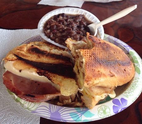 Cuban sandwich and black beans on a paper plate; toasted bread, ham, cheese, beans in a white bowl.