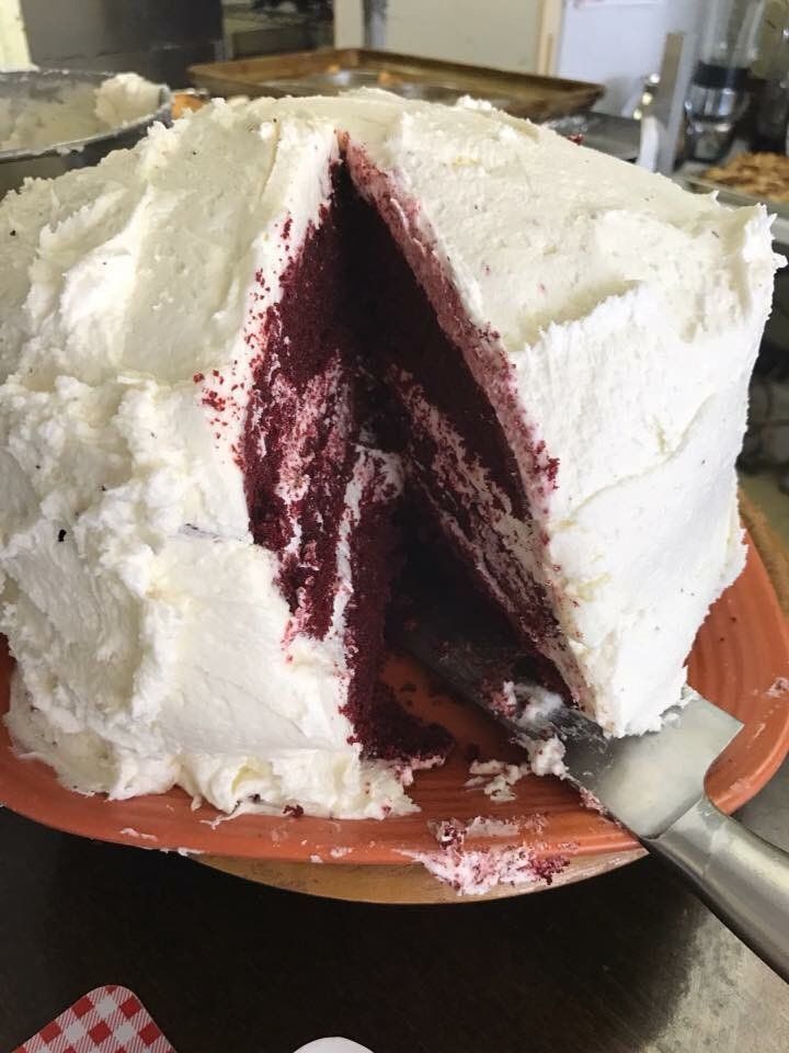 Red velvet cake with white frosting, slice removed, on an orange plate.