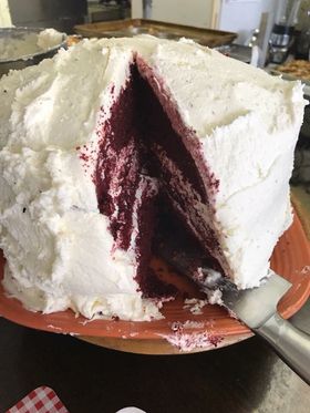 Red velvet cake with white frosting, slice removed, on an orange plate.