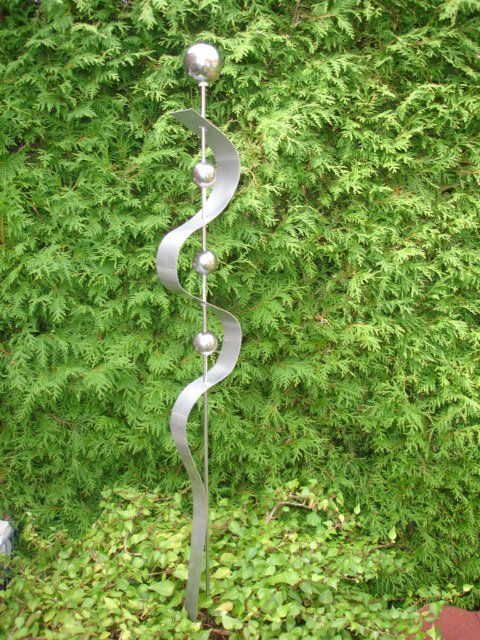 Eine Metallskulptur sitzt vor einem grünen Busch.