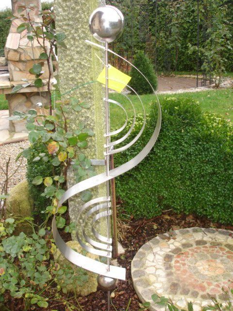 Eine Spiralskulptur aus Edelstahl steht inmitten eines Gartens.