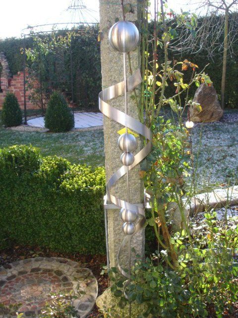 Eine Skulptur aus Edelstahl hängt an einem Baum in einem Garten