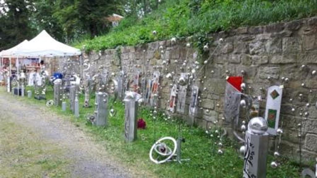 Eine Reihe von Skulpturen steht aufgereiht an einer Steinmauer.