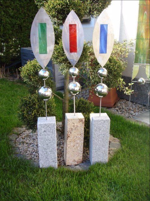 Drei Skulpturen sitzen auf Granitblöcken im Gras