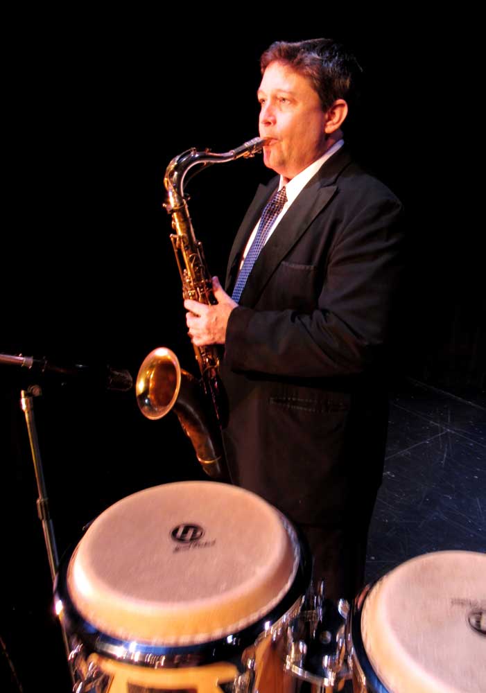 A man in a suit is playing a saxophone and drums