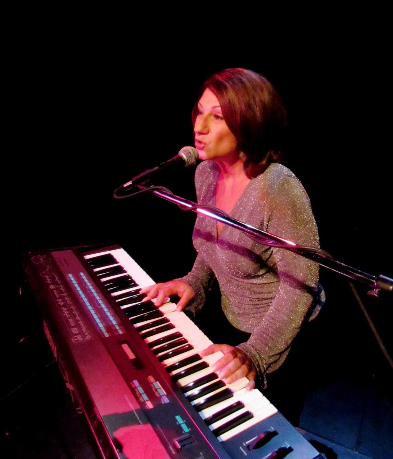 A woman singing into a microphone while playing a keyboard