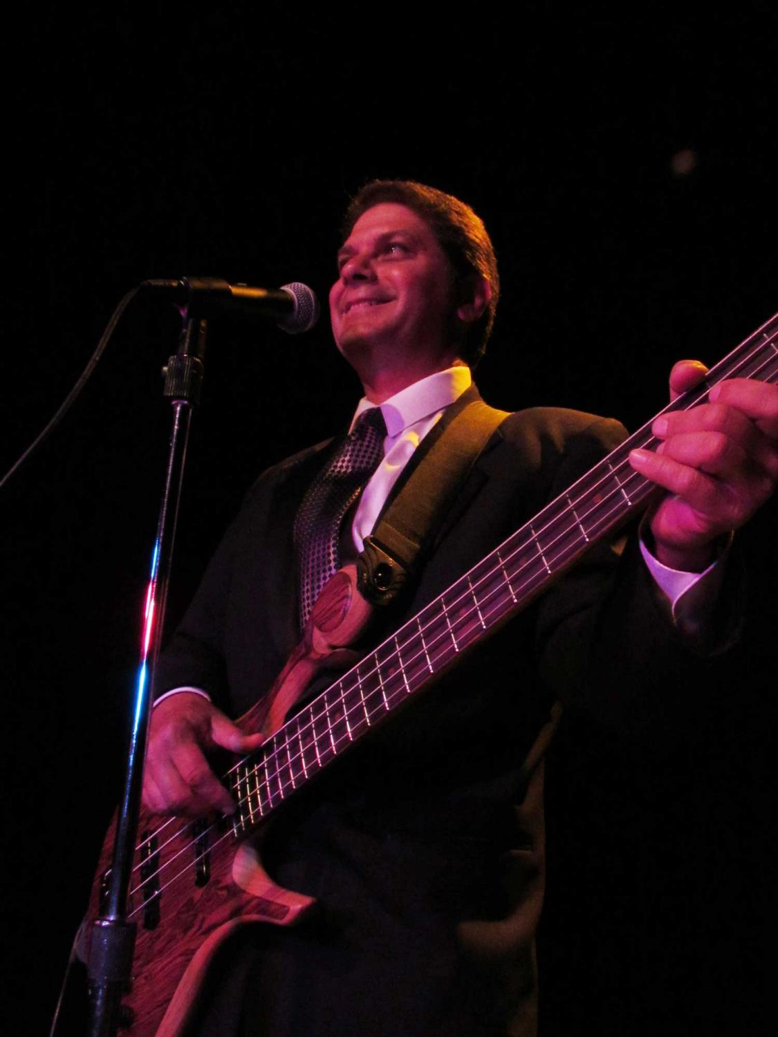 A man in a suit is playing a bass guitar and singing into a microphone