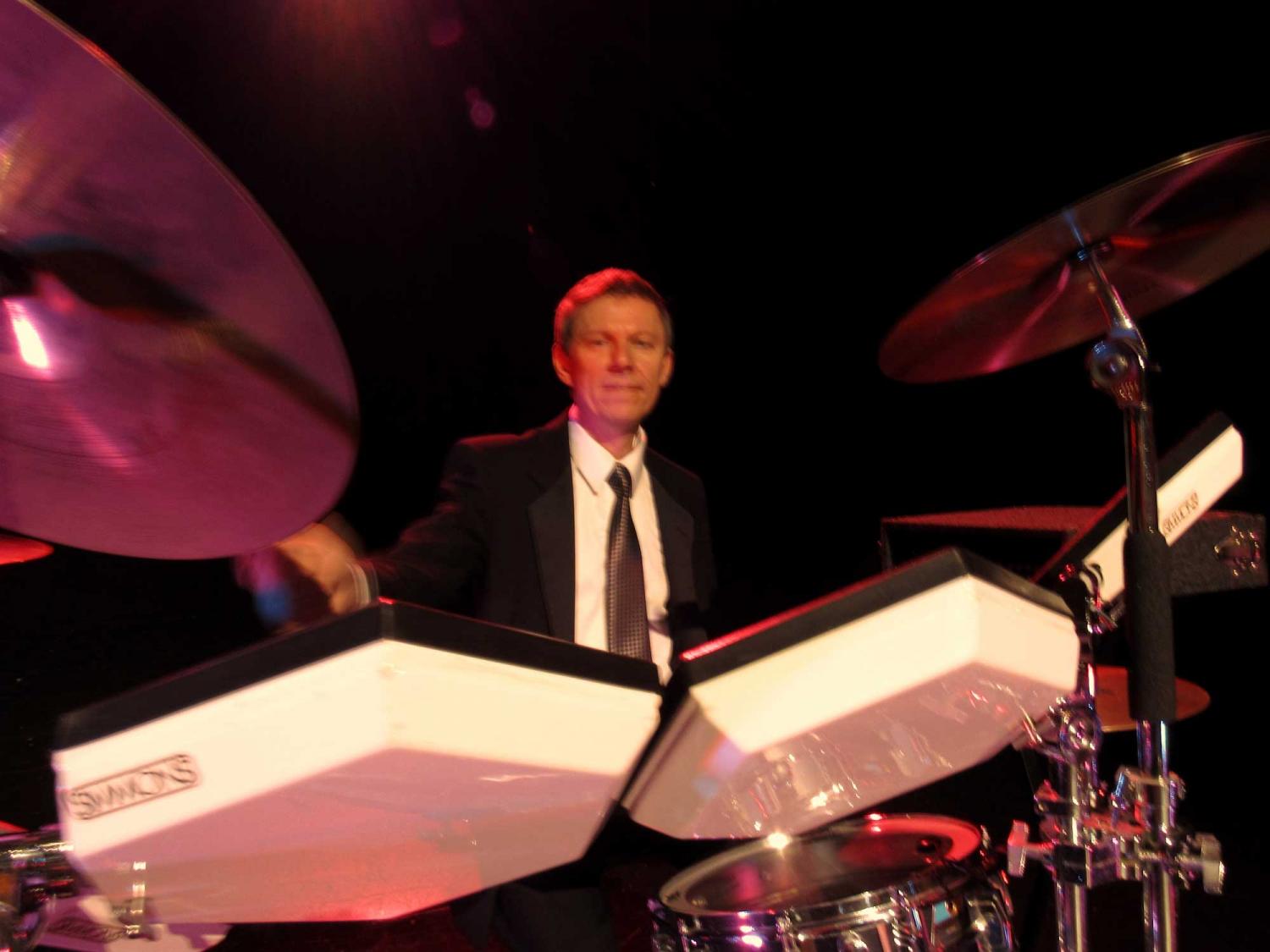 A man in a suit and tie is playing drums on a stage