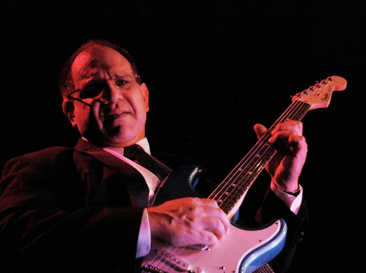 A man in a suit and tie is playing an electric guitar