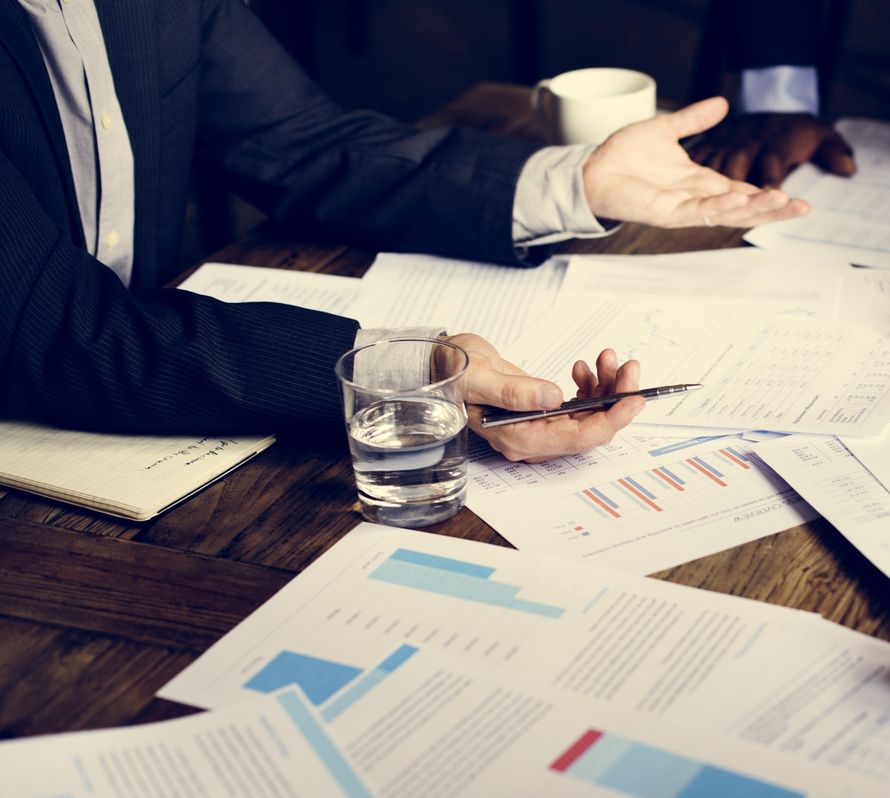 Business meeting with hands, coffee cup, water glass, and financial charts on a wooden table