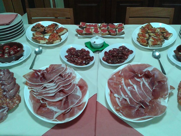 La tavola è imbandita con piatti di pane conditi con pomodoro, salumi e contorni.