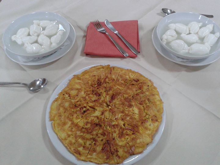 Una tavola apparecchiata con una frittata, due ciotole di mozzarella e posate.