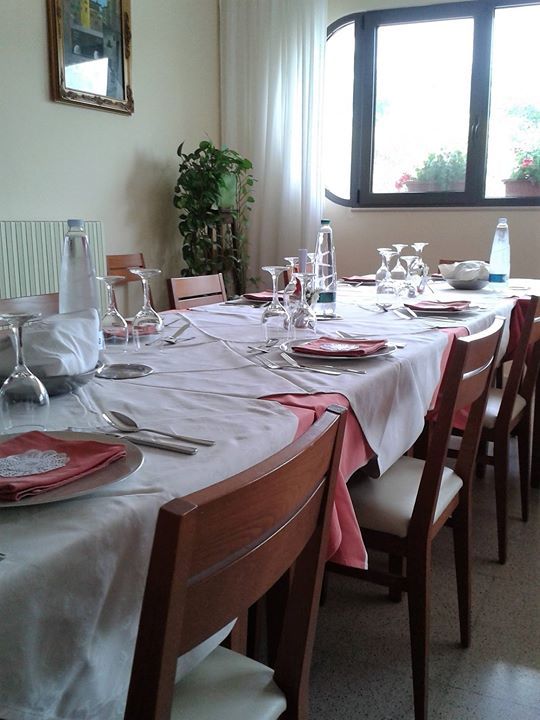 Tavolo da pranzo apparecchiato per un pasto, con tovaglia bianca e dettagli rosa, vicino a una finestra.