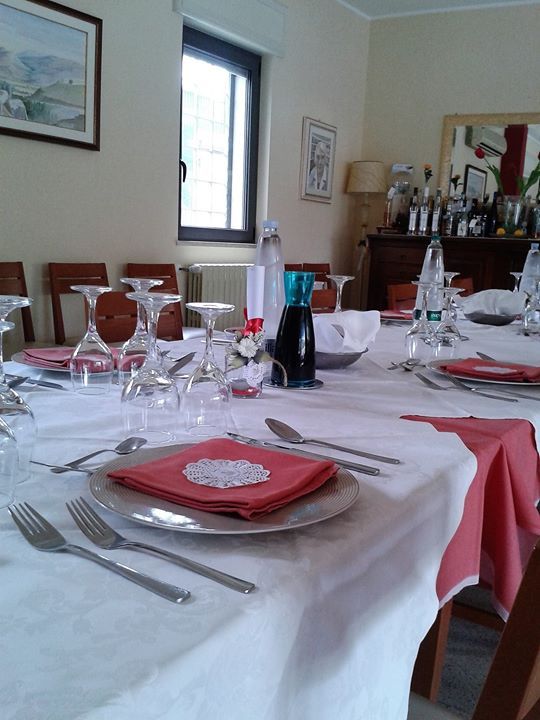 Un tavolo da pranzo apparecchiato per un pasto, con tovaglia bianca, piatti, posate e tovaglioli rossi.