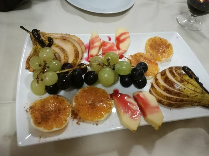Piatto di frutta con pere, uva, arance e mele, condito con salsa, su un piatto rettangolare bianco.