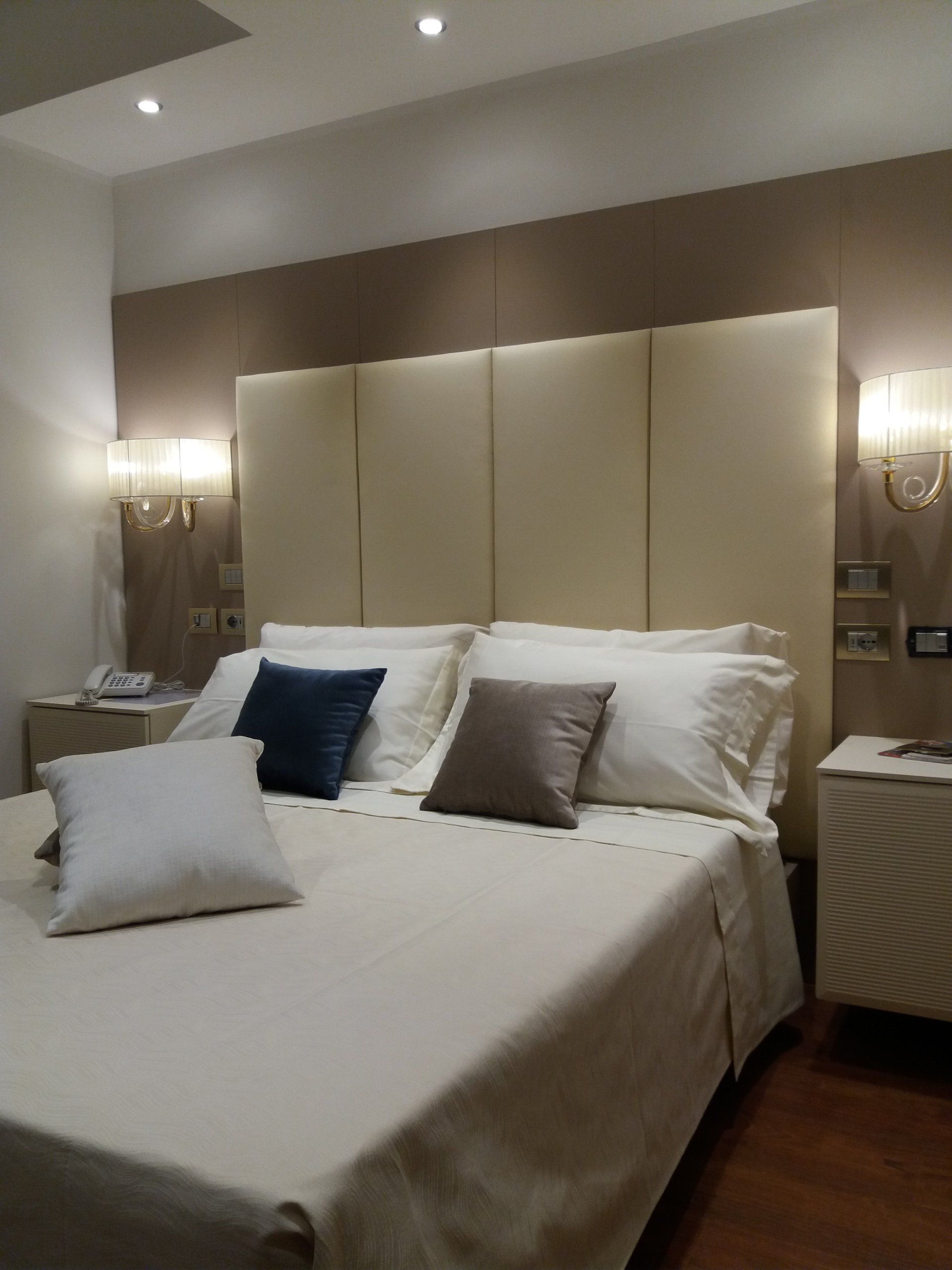 Camera da letto con biancheria da letto color crema, testiera e due comodini. Cuscini decorativi in blu, marrone e bianco.