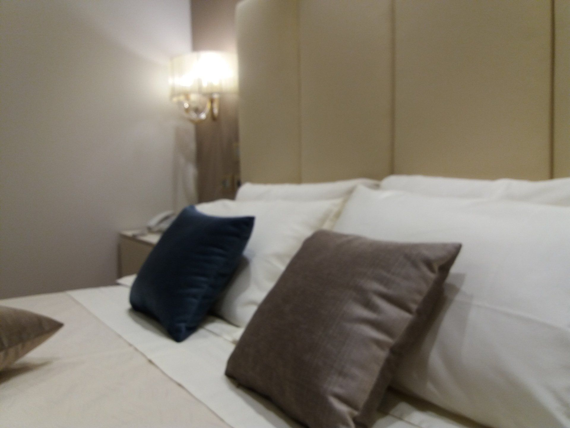 Letto con cuscini in una camera d'albergo; colori neutri, applique illuminata.