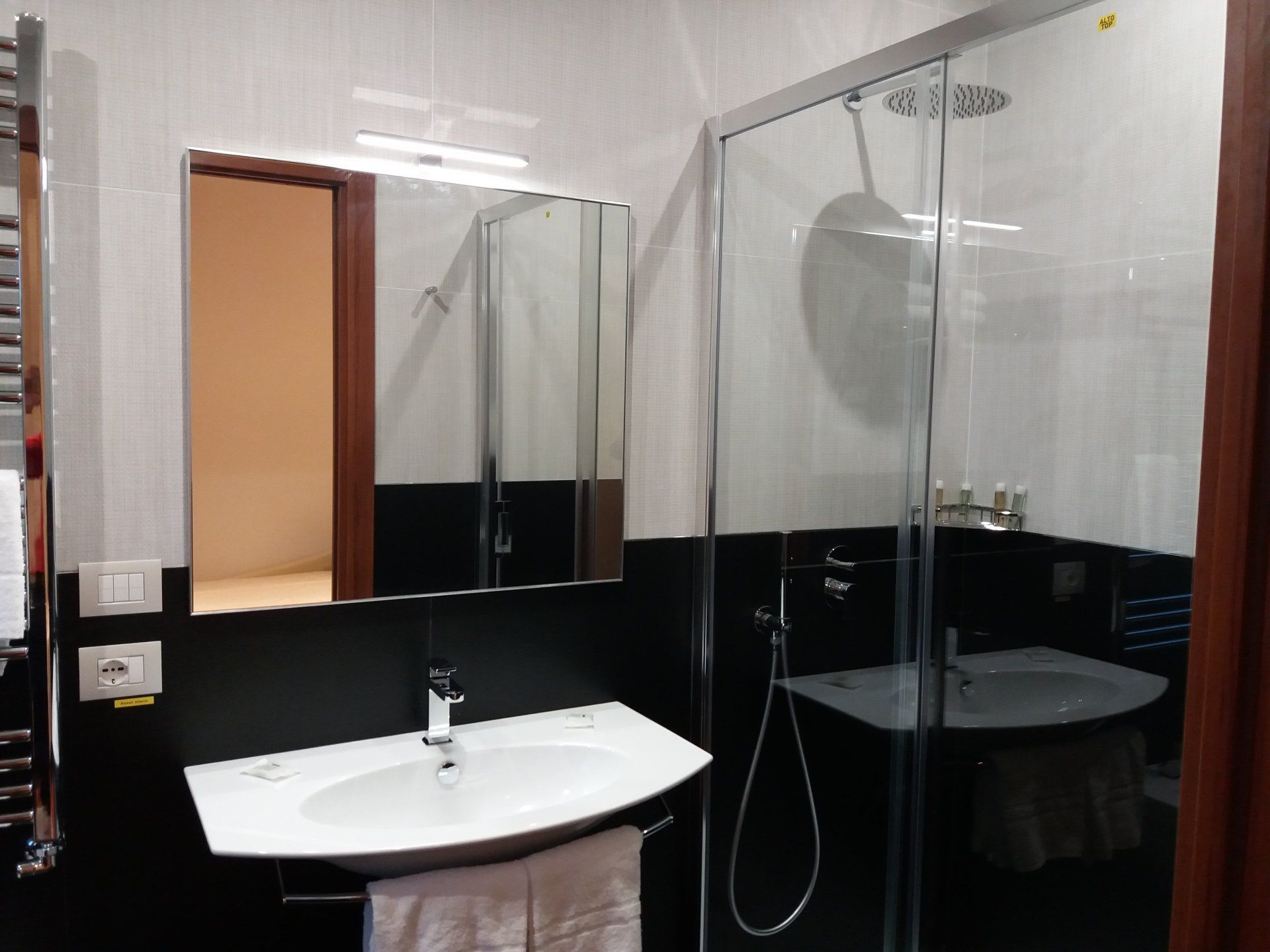 Bagno con piastrelle bianche e nere, doccia, lavandino e specchio.