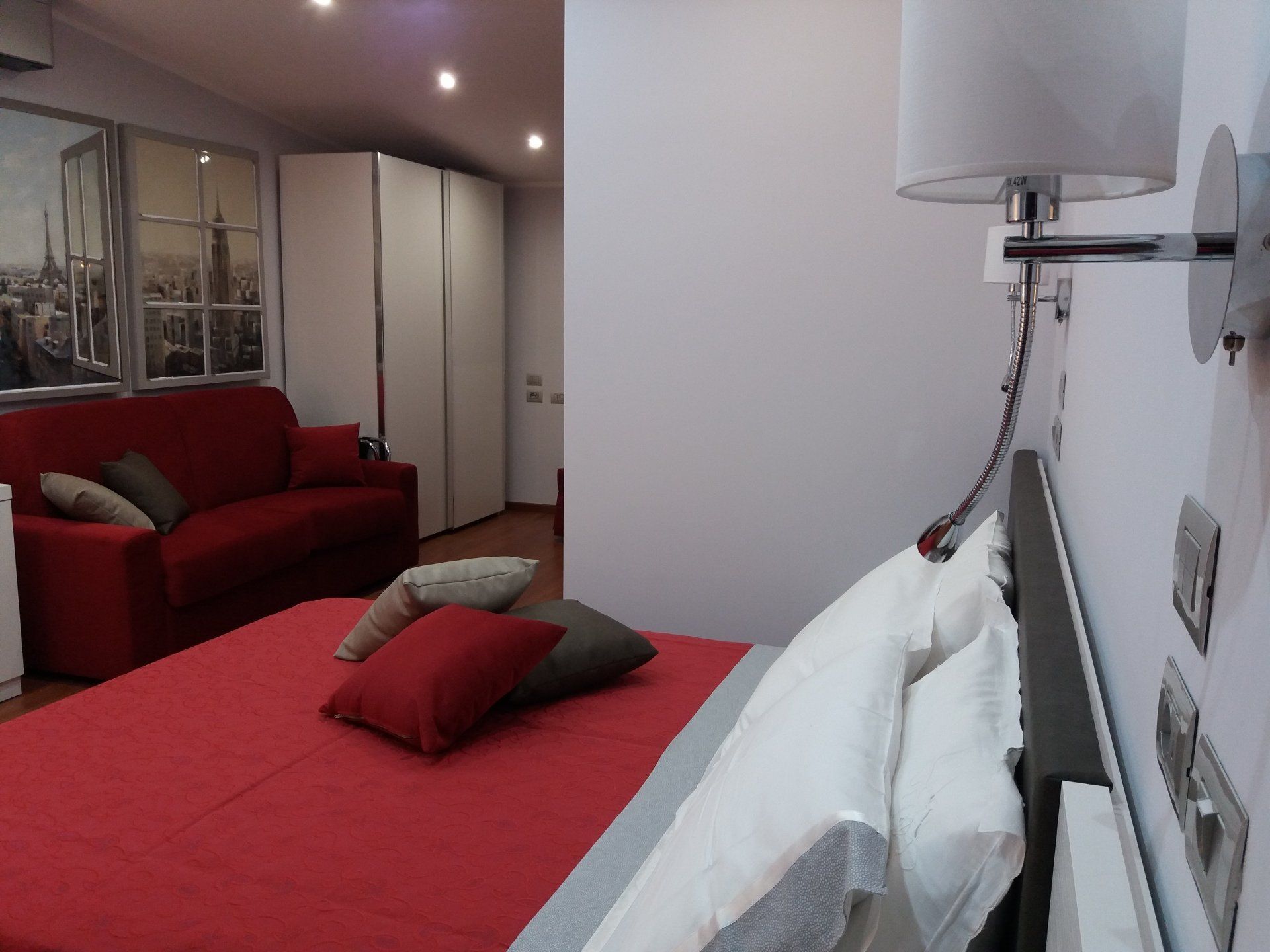 Camera da letto a tema rosso con letto, divano, opere d'arte e armadio bianco.