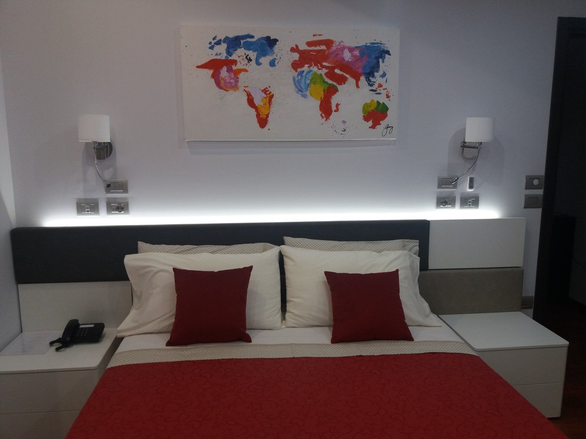 Camera da letto con letto, lenzuola e cuscini rossi, comodini e un'opera d'arte raffigurante una mappa del mondo.