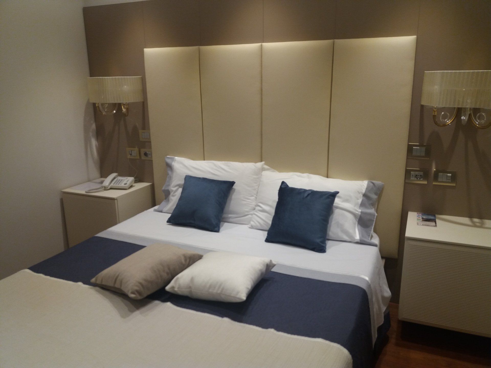 Camera da letto con un letto, due comodini, lampade e una grande testiera imbottita.