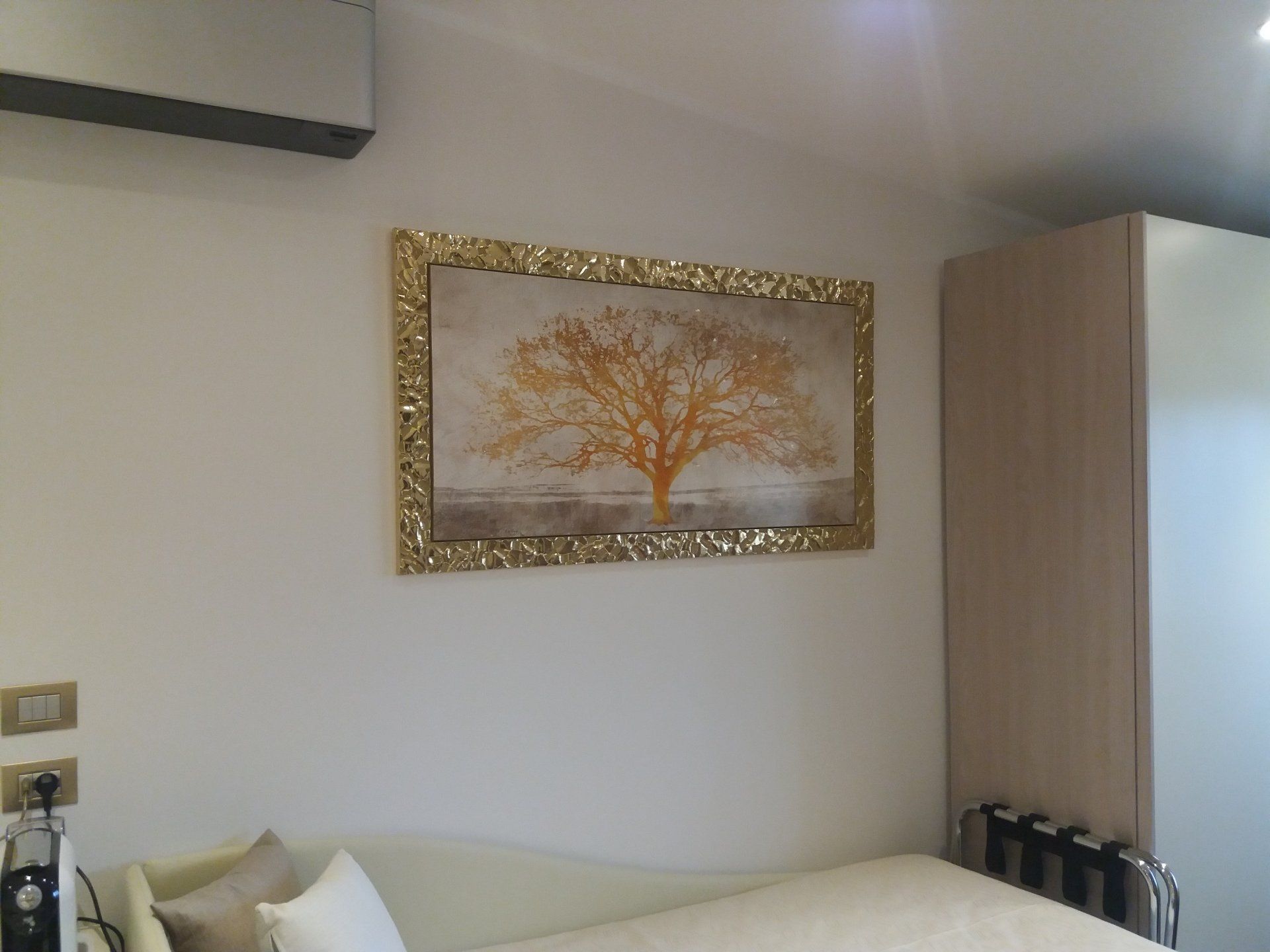 Parete con dipinto di un albero dorato, sopra un letto. Sulla destra c'è un armadio.