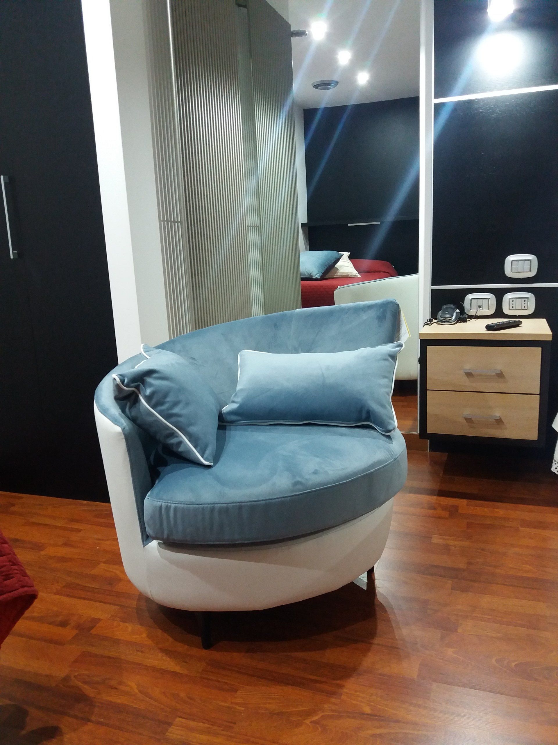 Poltrona curva blu e bianca con cuscino in una stanza moderna con pavimenti in legno e una parete riflettente.