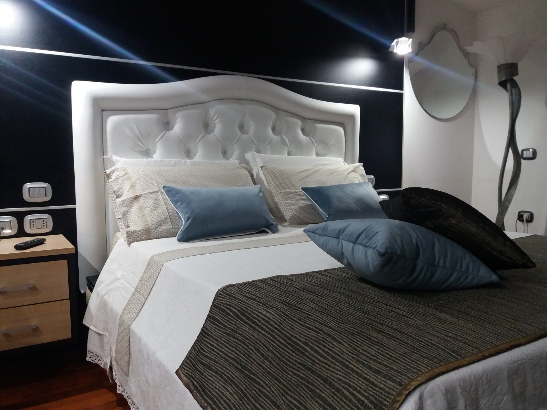 Camera da letto con testiera bianca trapuntata, cuscini blu e coperta marrone.
